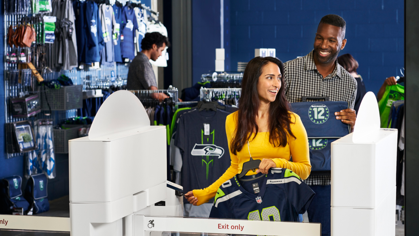 A man and a woman leaving the Seattle Seahawks stadium store using Just Walk Out to purchase sports shirts